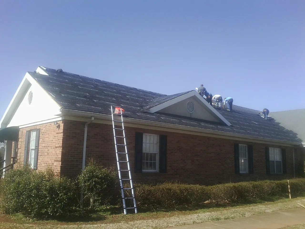 Crew tearing shingles off a brick ranch roof with a ladder set — Metal Roof Repair work by our crew in Woodridge
