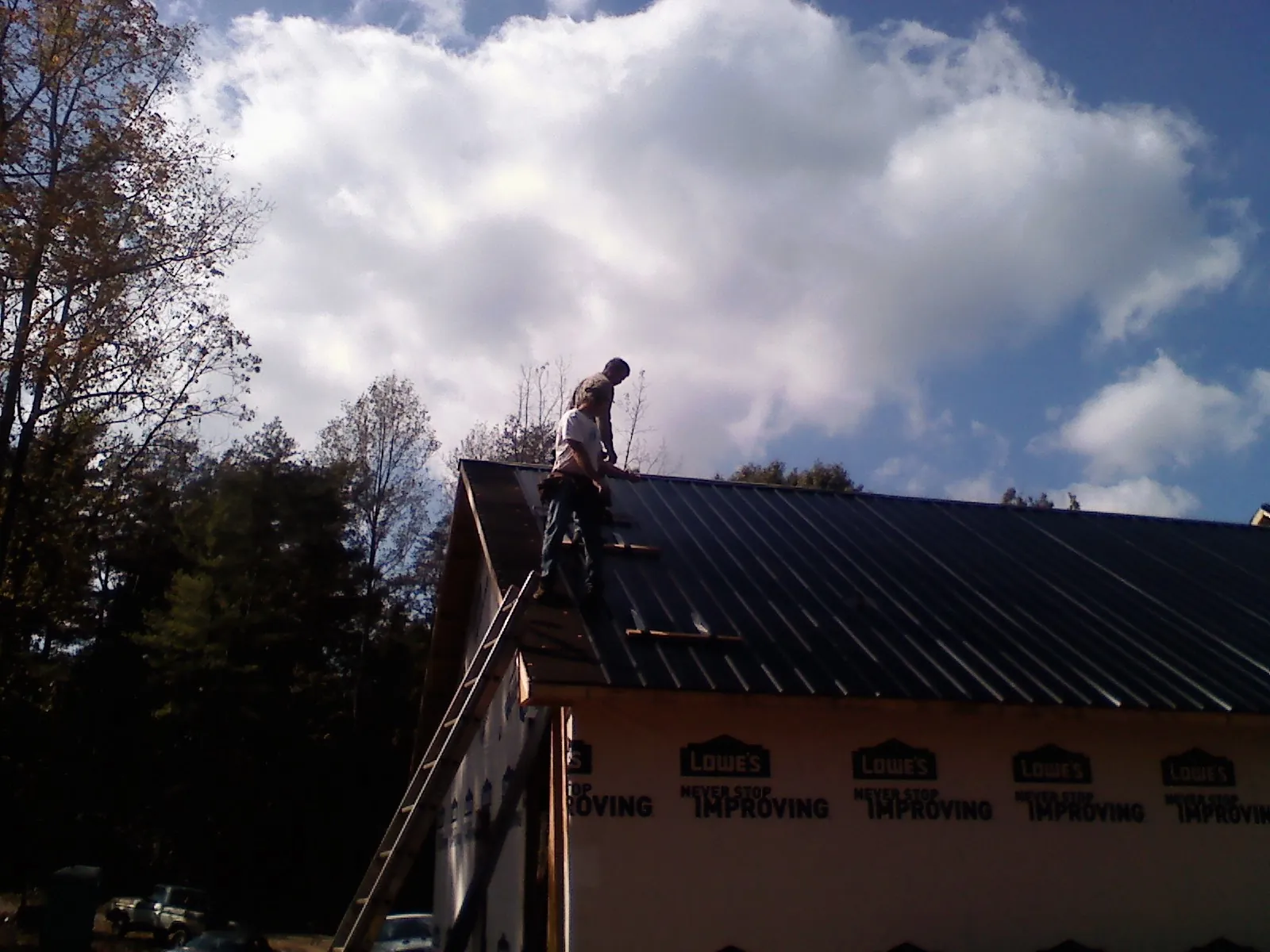 Roofer fastening dark metal panels high against a cloudy sky, from a Roof Inspection job in Woodridge