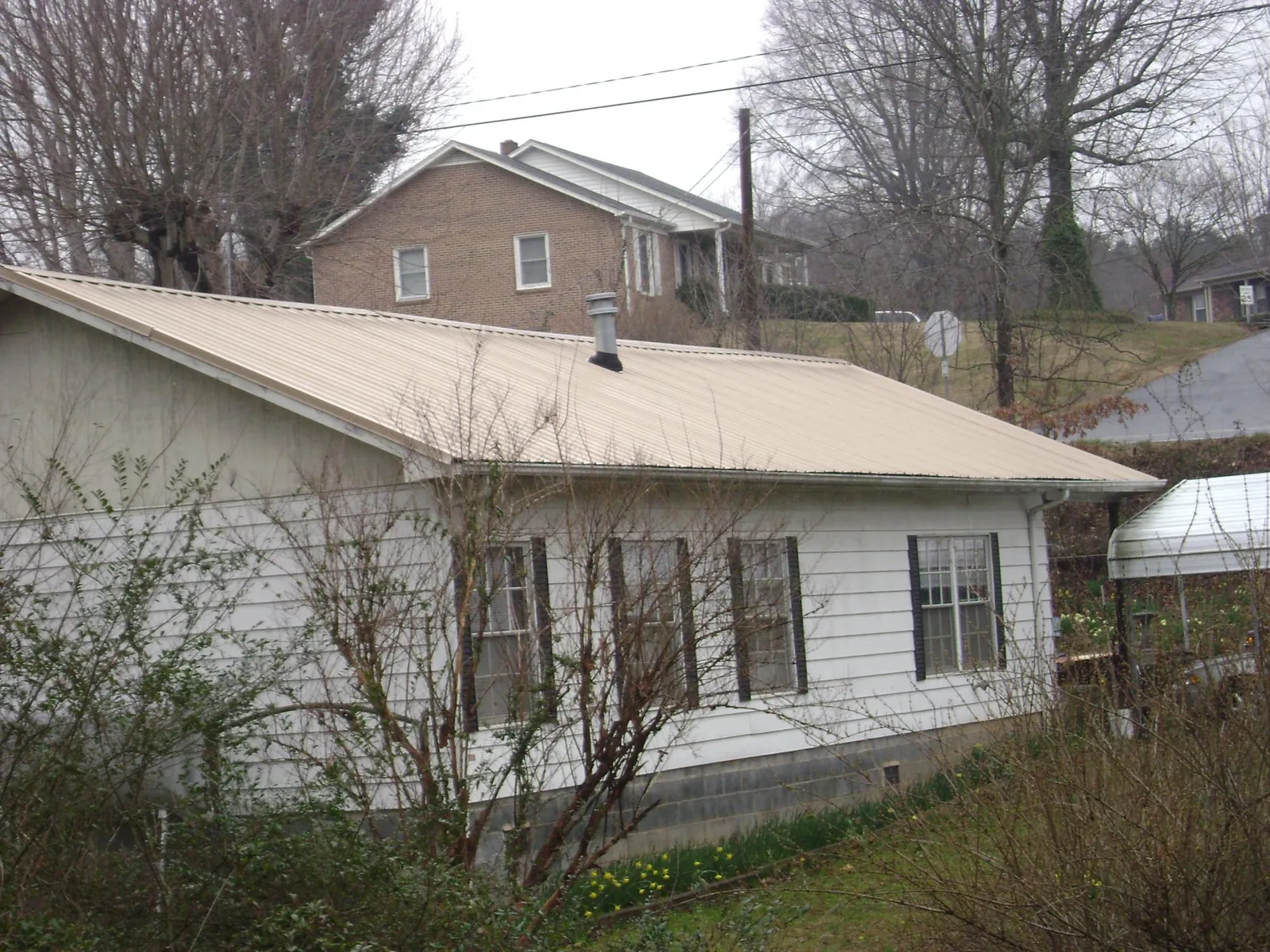 Tan metal roof on a white sided house set into a hillside — Commercial Roofing by Roofing Brothers in Woodridge